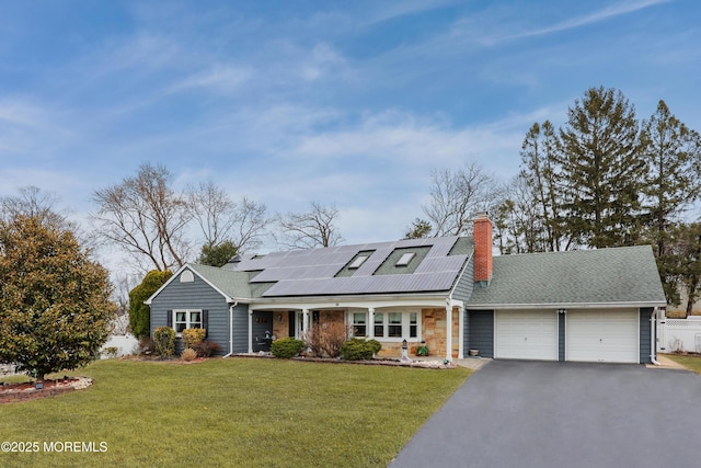 view of front of home with driveway, solar panels, a chimney, an attached garage, and a front yard