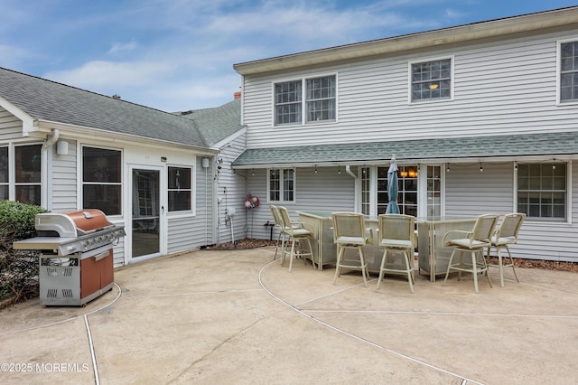 rear view of property featuring a patio, a shingled roof, and outdoor dining space