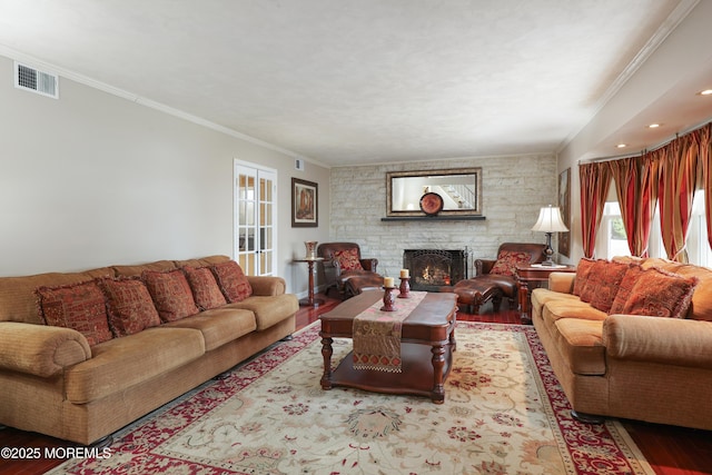 living area with visible vents, a fireplace, ornamental molding, and wood finished floors