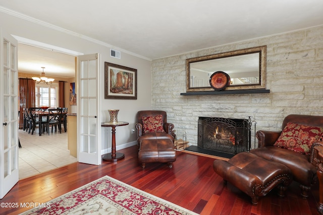 sitting room with visible vents, wood finished floors, crown molding, a fireplace, and a notable chandelier