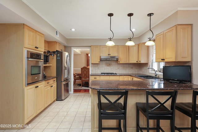 kitchen with appliances with stainless steel finishes, a sink, under cabinet range hood, and light brown cabinetry