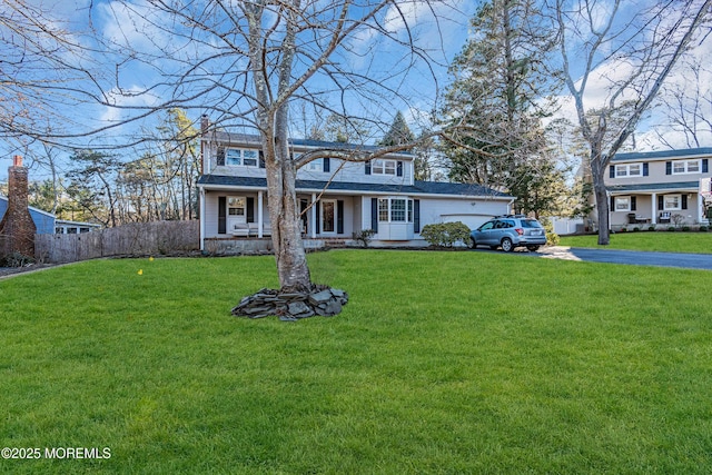 view of front of house featuring driveway, a garage, a chimney, a porch, and a front yard