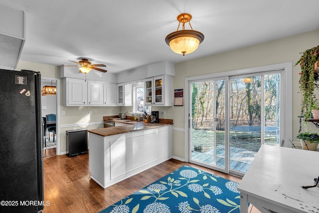 kitchen with a peninsula, dark wood-style floors, white cabinets, and freestanding refrigerator