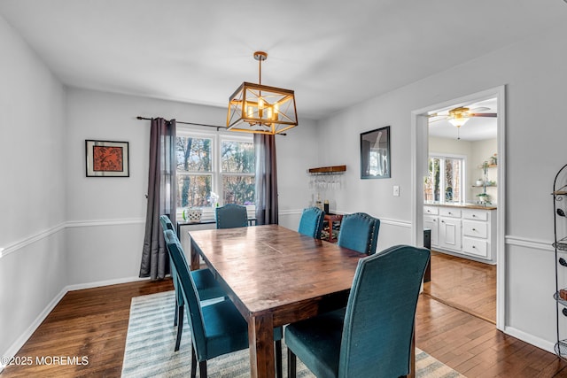 dining room with ceiling fan with notable chandelier, dark wood finished floors, and baseboards