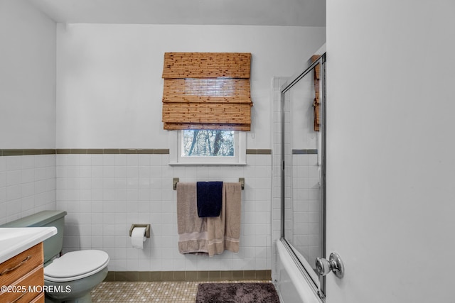 full bath featuring toilet, combined bath / shower with glass door, vanity, and tile walls