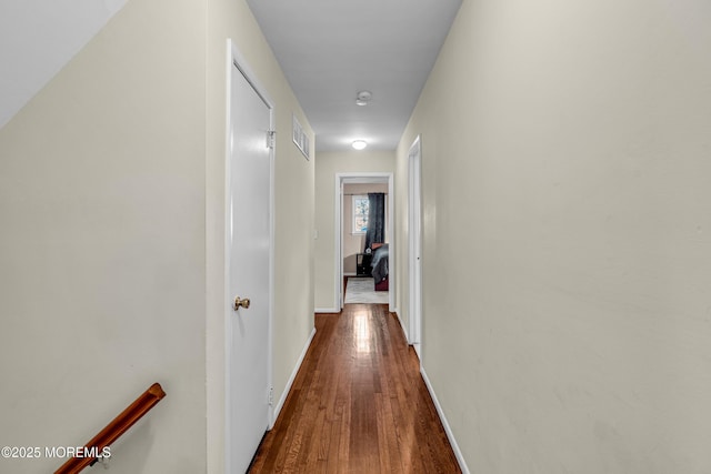 hall featuring dark wood-style flooring, visible vents, and baseboards