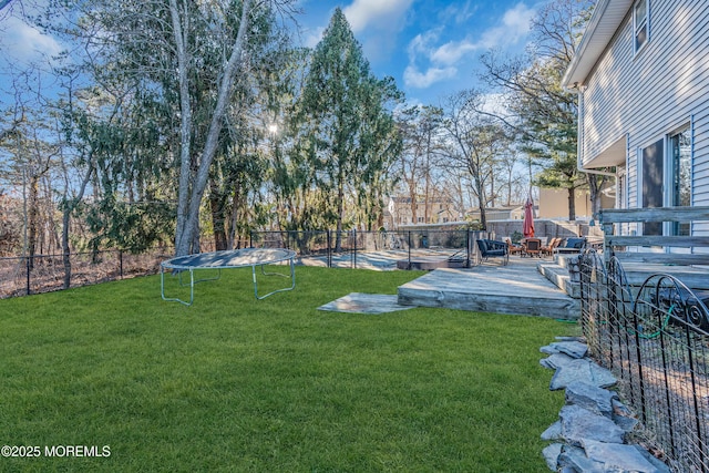 view of yard featuring a trampoline, a fenced backyard, and a wooden deck