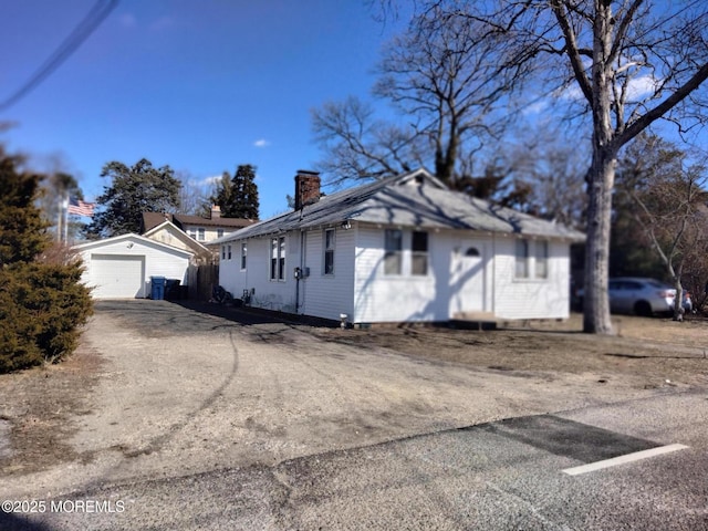 view of side of property with driveway, a chimney, an outdoor structure, and a detached garage