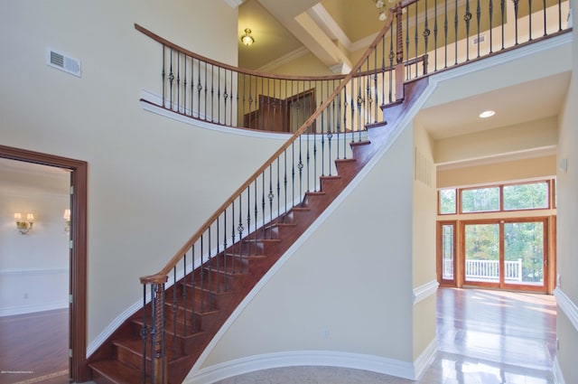 stairs with crown molding, visible vents, a high ceiling, wood finished floors, and baseboards