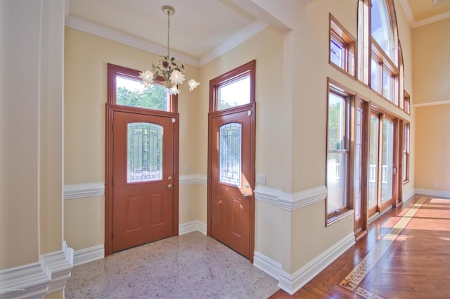 entrance foyer featuring wood finished floors, a towering ceiling, baseboards, an inviting chandelier, and crown molding