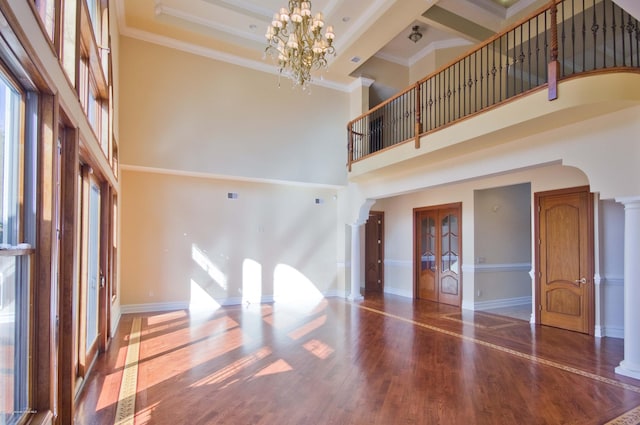 unfurnished living room featuring a notable chandelier, crown molding, wood finished floors, and ornate columns