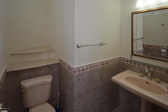 bathroom with toilet, a sink, tile walls, and wainscoting