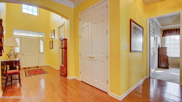 foyer entrance featuring ornamental molding, arched walkways, baseboards, and light wood finished floors