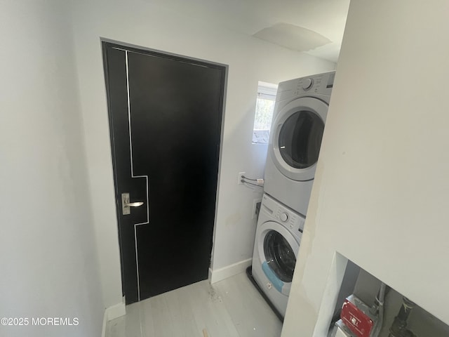 laundry room with light wood finished floors, laundry area, baseboards, and stacked washer and dryer