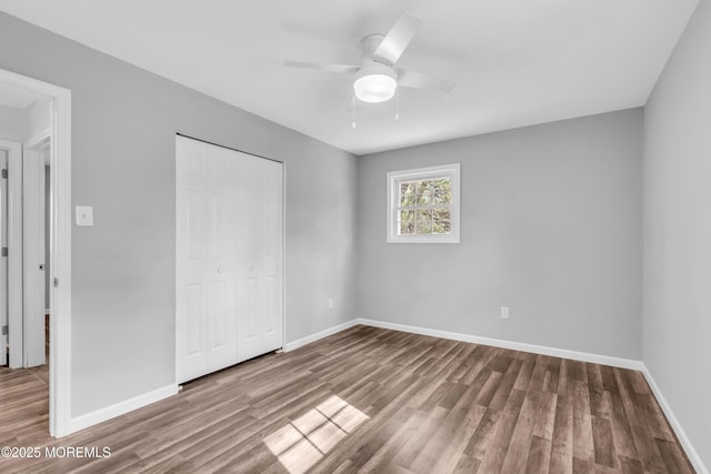 unfurnished bedroom with ceiling fan, a closet, wood finished floors, and baseboards