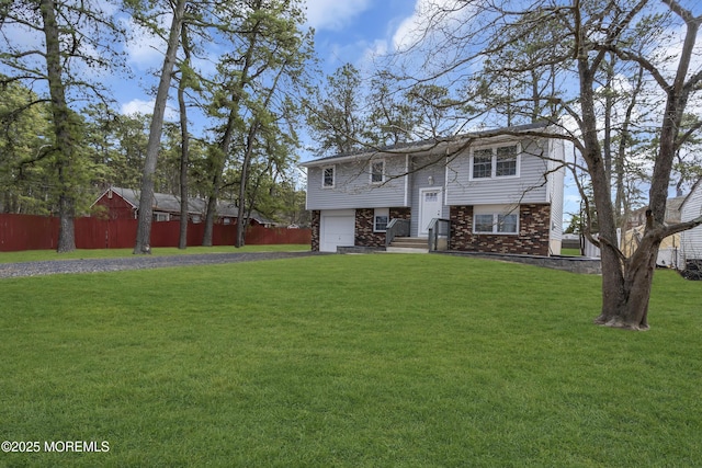 view of front facade featuring a garage, driveway, brick siding, fence, and a front yard