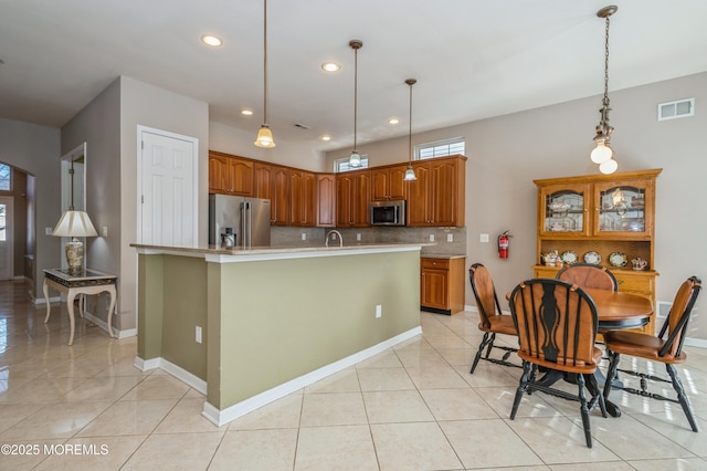 kitchen with a center island with sink, visible vents, appliances with stainless steel finishes, brown cabinets, and light countertops