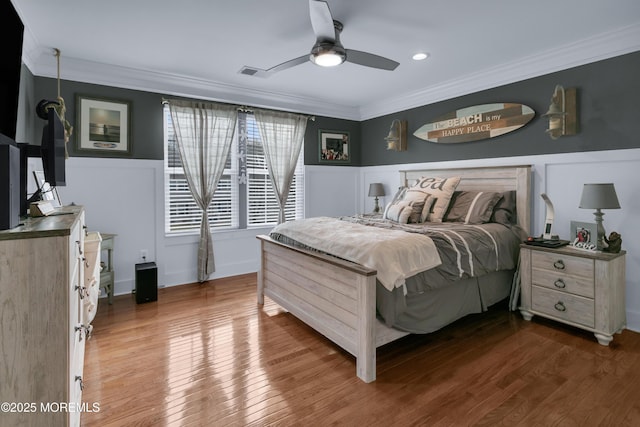 bedroom featuring ornamental molding, wainscoting, visible vents, and wood finished floors