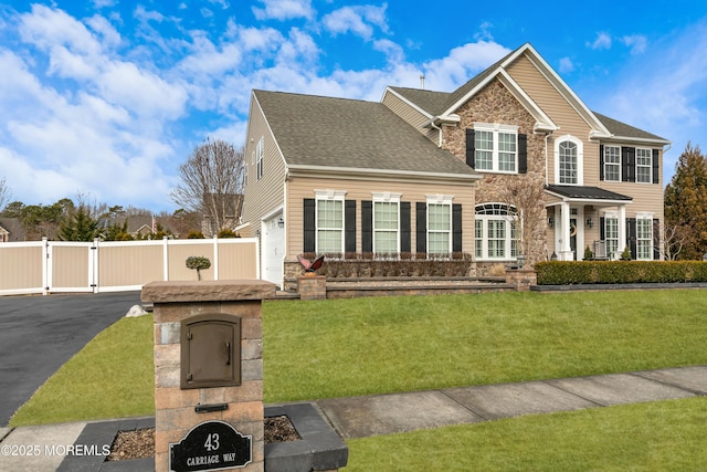 view of front of house featuring aphalt driveway, a front yard, stone siding, and a gate