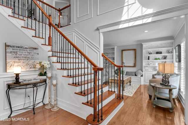 staircase with ornamental molding, wood finished floors, built in features, and a decorative wall