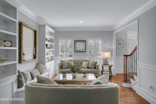 living room featuring a wainscoted wall, wood finished floors, stairs, crown molding, and a decorative wall