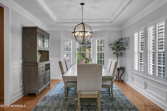 dining room with light wood-type flooring, an inviting chandelier, a raised ceiling, and a decorative wall