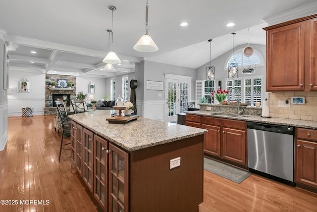 kitchen featuring a stone fireplace, a sink, open floor plan, stainless steel dishwasher, and wainscoting