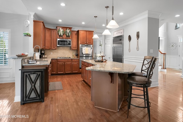 kitchen with light stone counters, appliances with stainless steel finishes, backsplash, brown cabinetry, and a kitchen bar