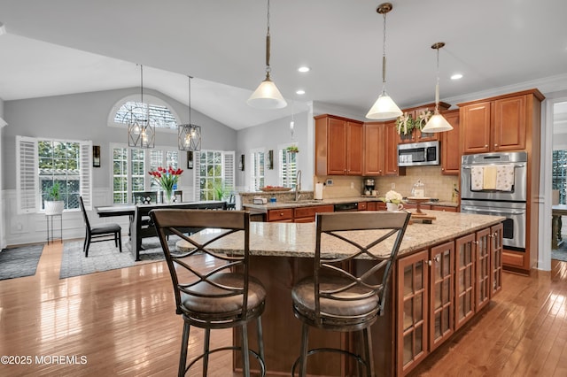 kitchen with appliances with stainless steel finishes, brown cabinetry, a sink, and light stone counters