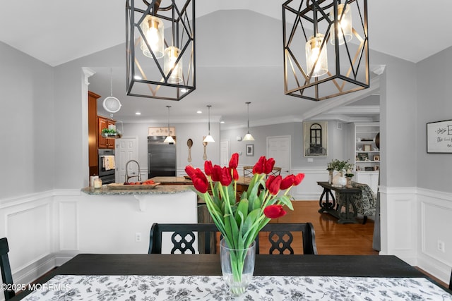 dining space with lofted ceiling, a decorative wall, wood finished floors, and wainscoting