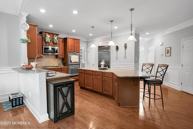 kitchen with a breakfast bar area, backsplash, appliances with stainless steel finishes, brown cabinetry, and light stone countertops