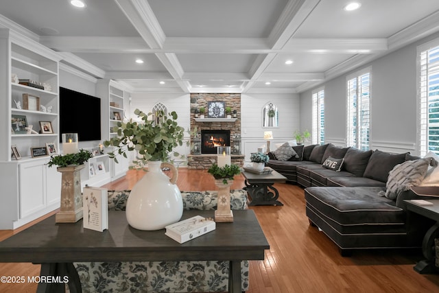 living area featuring beam ceiling, crown molding, a stone fireplace, wood finished floors, and coffered ceiling