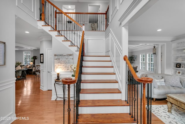 stairs featuring wainscoting, a decorative wall, crown molding, and wood finished floors