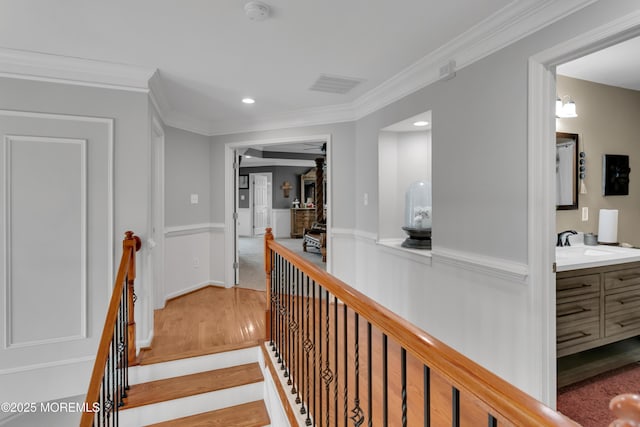 hallway with a sink, wood finished floors, visible vents, ornamental molding, and wainscoting