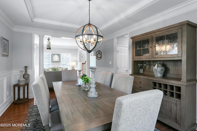 dining space with a wainscoted wall, ornamental molding, dark wood-style flooring, a chandelier, and a decorative wall