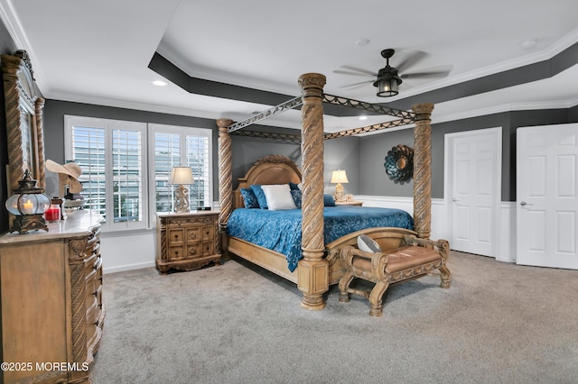 bedroom with a tray ceiling, ornamental molding, wainscoting, carpet flooring, and ceiling fan