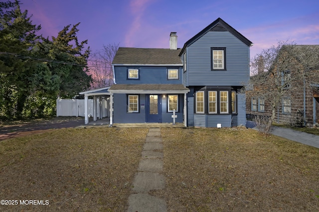 rear view of house with a shingled roof, a chimney, and a lawn