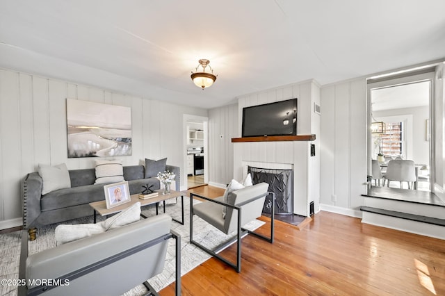 living area featuring a large fireplace, baseboards, and wood finished floors