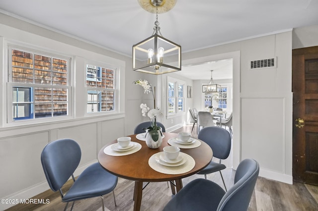 dining space with visible vents, ornamental molding, wood finished floors, a chandelier, and a decorative wall