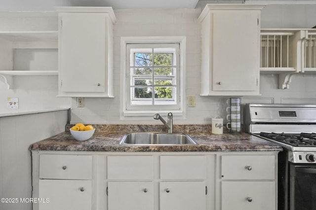 kitchen with stainless steel gas range oven, dark countertops, a sink, and white cabinetry