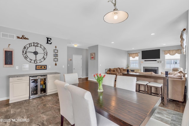 dining space with baseboards, visible vents, wine cooler, a bar, and a fireplace