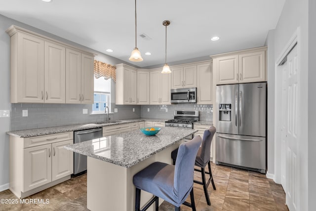 kitchen featuring appliances with stainless steel finishes, light stone counters, a center island, hanging light fixtures, and a sink