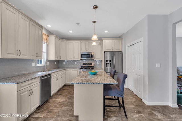 kitchen featuring a kitchen island, appliances with stainless steel finishes, a breakfast bar, light stone counters, and pendant lighting