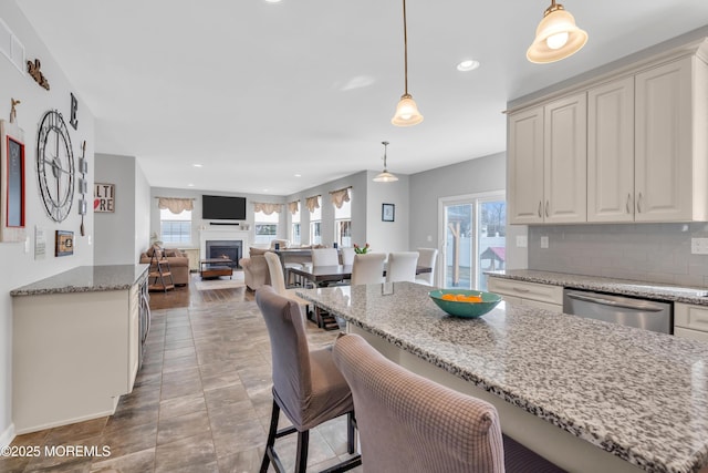 kitchen featuring decorative backsplash, light stone counters, decorative light fixtures, a lit fireplace, and stainless steel dishwasher