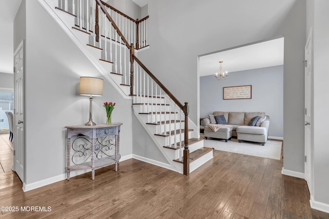 stairway featuring a towering ceiling, baseboards, a chandelier, and hardwood / wood-style floors