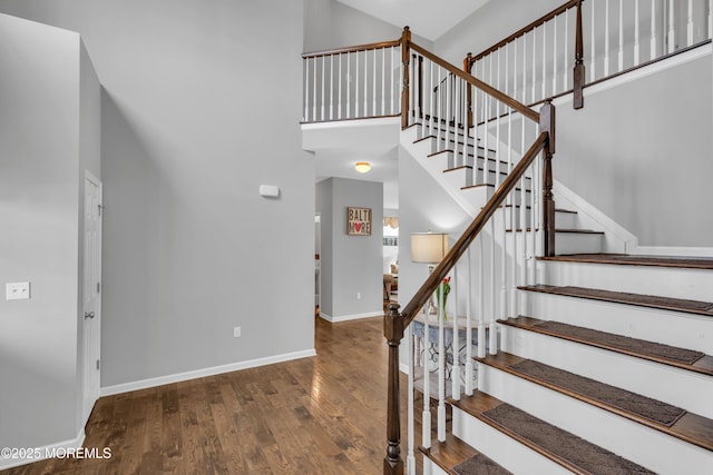 stairs featuring wood finished floors, a towering ceiling, and baseboards