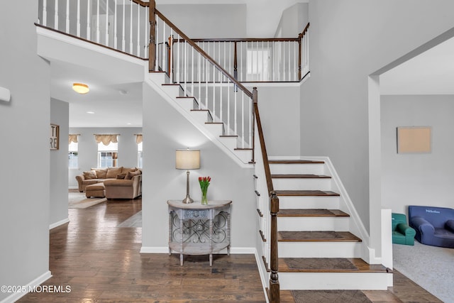 stairs featuring wood-type flooring, a high ceiling, and baseboards