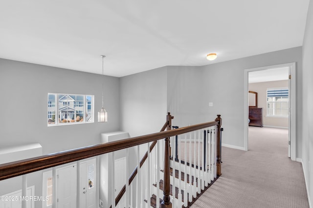 hall featuring an inviting chandelier, baseboards, light colored carpet, and an upstairs landing