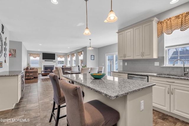 kitchen featuring a warm lit fireplace, a sink, open floor plan, hanging light fixtures, and dishwasher