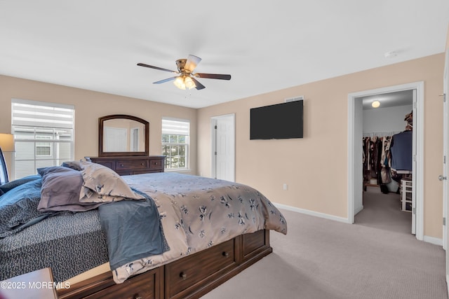 bedroom featuring light carpet, a spacious closet, ceiling fan, and baseboards